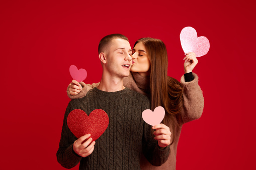 Portrait of beautiful, happy young couple, man and woman posing, having fun against red studio background. Concept of love, relationship, Valentine's Day, emotions, lifestyle