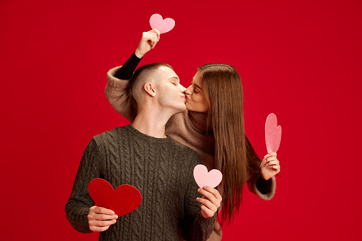 Portrait of beautiful, happy young couple, man and woman posing, having fun against red studio background. Concept of love, relationship, Valentine's Day, emotions, lifestyle