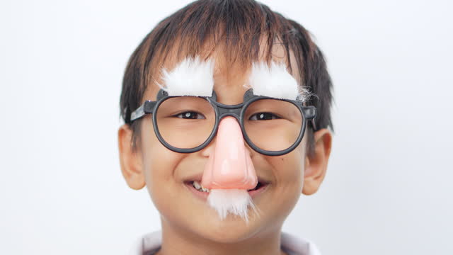 Boy wearing clown glasses fake nose mustache and eyebrows looks at camera and makes a facial expression.