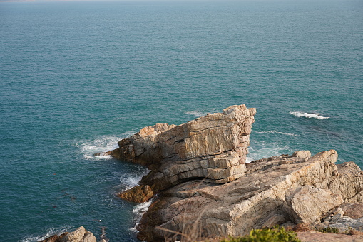 A mesmerizing shot of the endless sea meeting colossal rocks, where waves crash gracefully against the rugged shoreline