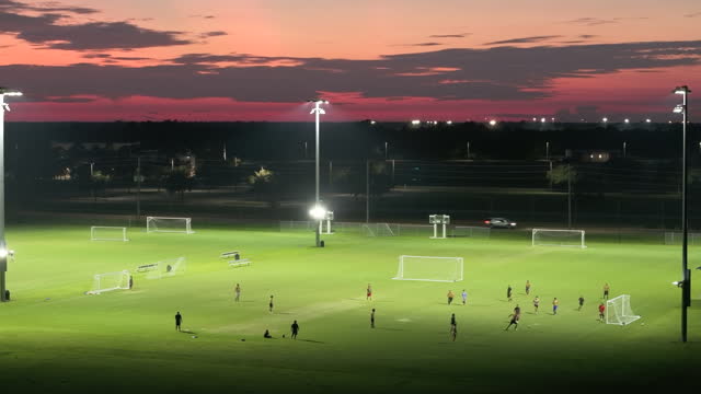 Sportsmen playing football game on illuminated stadium in public sports park at night