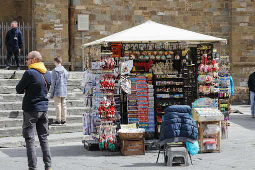 Florence, Italy - April 14, 2023: There is a stall on the pavement in the historic centre selling maps, souvenirs and other small items.  Next to this stall, several people are looking in another direction, not at the items on sale.