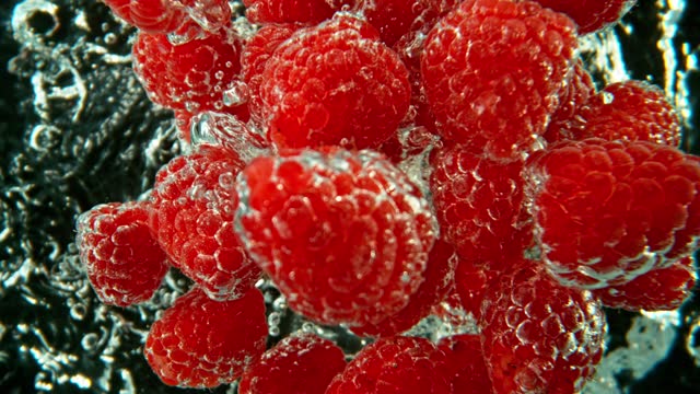Super Slow Motion of Falling Raspberries Into Water on Black Background.