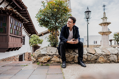 Young man looking around and holding mobile phone on a colonial old town city