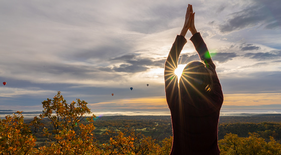 Woman meditating at sunrise in the mountain with hot air balloons flying in the background