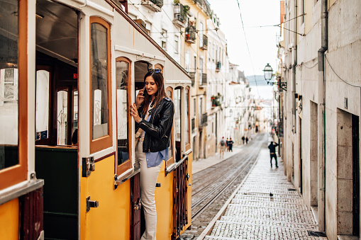 A beautiful young woman is riding a tram and talking with someone using her smart phone. She also enjoying in a beautiful view of eye catching old European city architecture.