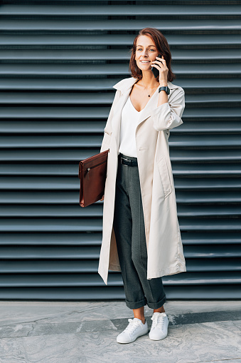 Full length of a stylish businesswoman with a folder talking on a mobile phone outdoors