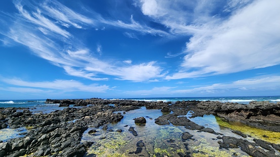 Wide angle view of rocky beach with strong winds, waves and cloudy sky, Kaʻena Point State Park, Oahu island, Hawaii