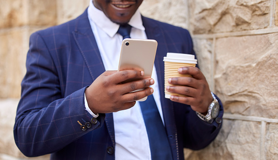 Travel, coffee and hands of businessman with phone on walk commute for social media, email or ecommerce. Technology, internet and corporate black man on outdoor break with 5g mobile connection.