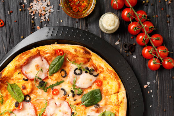 istock Pizza with ham on a black baking dish on a dark wooden background, top view. 1809894946
