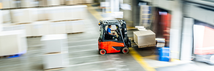Forklift driver transporting cargo box in warehouse, long exposure top view