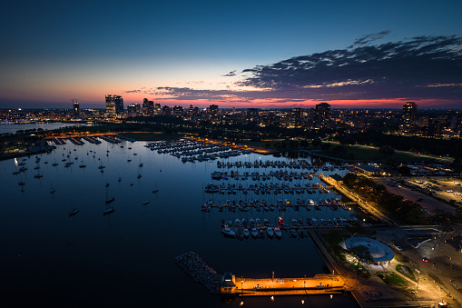 Drone shot of Milwaukee, Wisconsin at twilight on a Fall evening, flying over sailboats in multiple marinas and looking over Veterans Park towards apartment buildings on the Lower East Side and Yankee Hill and the downtown office buildings of Juneau Town.