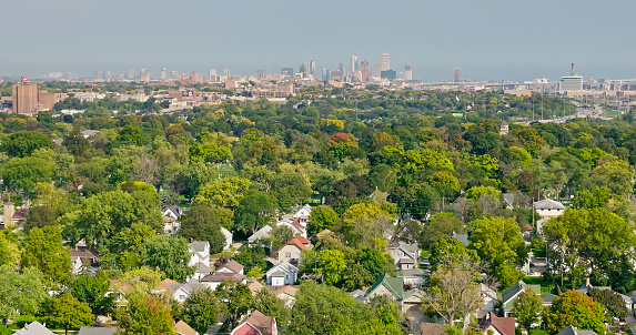 Aerial shot of Milwaukee, Wisconsin on a hazy day in Fall, looking across leafy residential streets in Bluemound Heights towards the downtown skyline, with Lake Michigan in the distance.