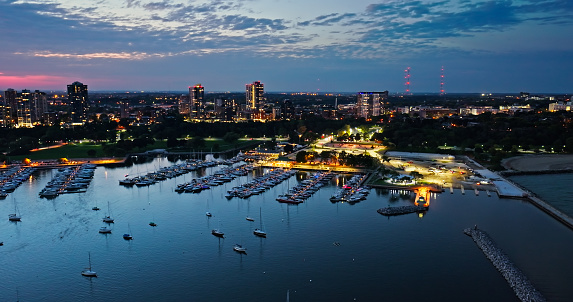 Aerial shot of Milwaukee, Wisconsin at twilight on a Fall evening, flying over sailboats in multiple marinas and looking over Veterans Park towards apartment buildings in the Lower East Side and Northpoint.