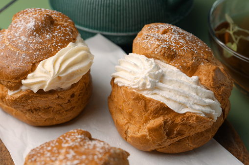 Delicious profiteroles filled with cream and tea on green background, closeup