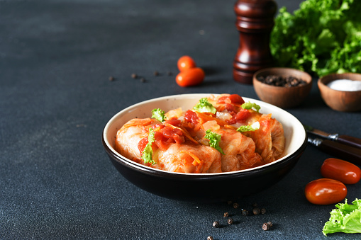 Stuffed cabbage rolls with meat and rice, with tomato souce in a plate on a dark background