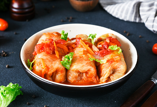 Stuffed cabbage rolls with meat and rice, with tomato souce in a plate on a dark background