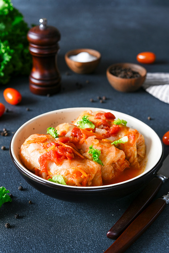 Stuffed cabbage rolls with meat and rice, with tomato souce in a plate on a dark background