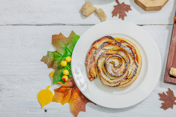 Apple roses pie with sugar powder. Traditional autumn baking, fall decor, flat lay. Hard light, dark shadow, wooden background, top view