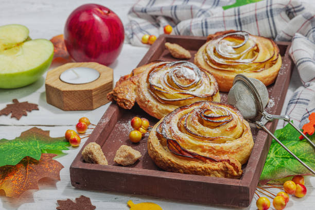 Apple roses pie with sugar powder. Traditional autumn baking, fall decor, flat lay. Hard light, dark shadow, wooden background, close up