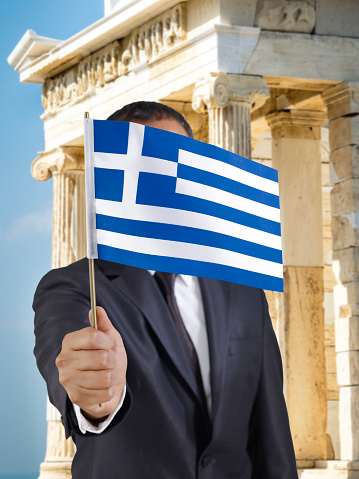 Businessman holding a Greek flag in front of Parthenon in Athens