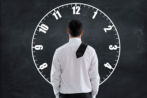 Rear view of a businessman looking at a blackboard with clock face