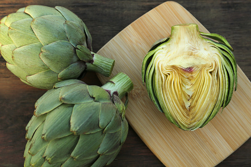 Whole and cut fresh raw artichokes on wooden table, flat lay