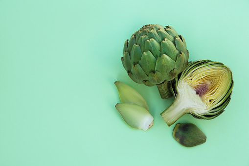 Whole and cut fresh raw artichokes on pale turquoise background, flat lay. Space for text