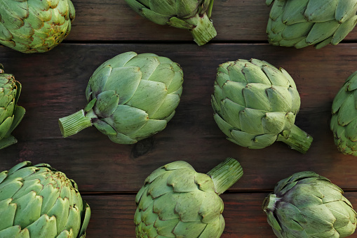 Whole fresh raw artichokes on wooden table, flat lay