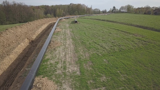 Laying gas pipeline among green hills. Large high-pressure steel pipes prepared for immersion in the excavated trench. Land works in the strategic industry. Energy and natural resources