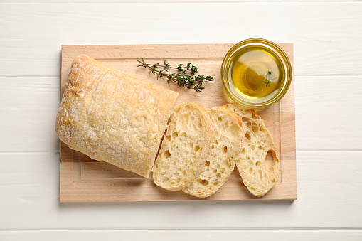 Bowl of olive oil, thyme and bread on white wooden table, flat lay