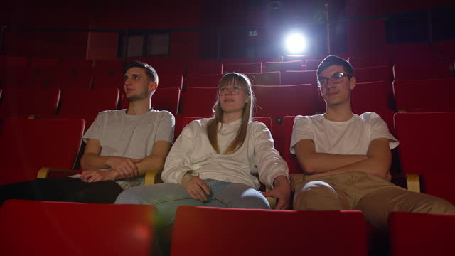 Nervous girl sitting between two boys in the cinema auditorium, handheld shot