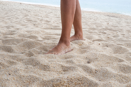 Male feet walk on white sand on the seashore. Rest and relaxation at a seaside resort.