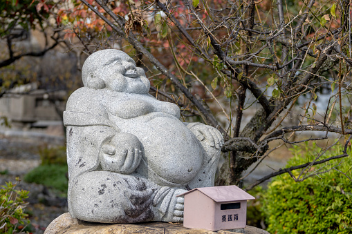 Nagahama, Shiga Prefecture, Japan. Nov 21, 2023. A sitting smiling Buddha stone figure at a Japanese a Shinto shrine.