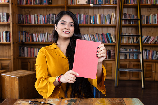 A beautiful young girl business woman or student working or studying holding a book in school or collage library or office