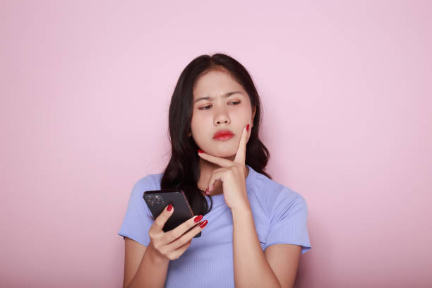 young woman using the mobile with a serious expression, portrait of a beautiful young woman in a light pink background, asian woman posing using a mobile phone. - news of the world imagens e fotografias de stock