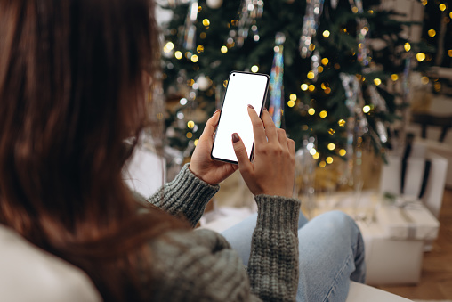 christmas mockup with space for text. christmas advertising, app template. hands holding phone with empty screen on background of golden beautiful christmas tree with lights in evening
