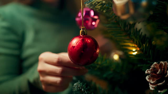 Merry Christmas and Happy New Year celebration, People hanging colorful small balls, bells and gift boxes on Christmas tree in living room, People decorating Christmas tree at home, Home interior with Christmas tree and sparkling lights