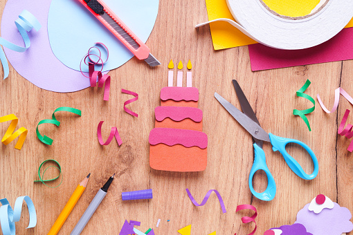 Paper birthday cake, confetti and stationery on wooden table, flat lay