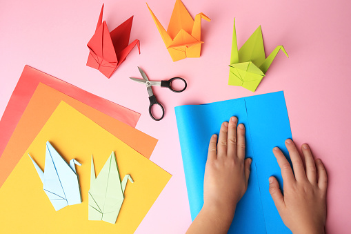 Origami art. Child folding paper on pink background, closeup and top view