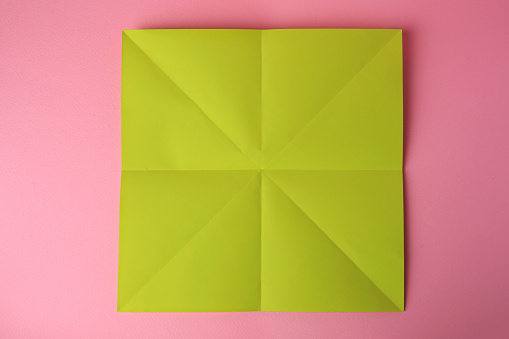 Origami art. Sheet of color paper on pink background, top view