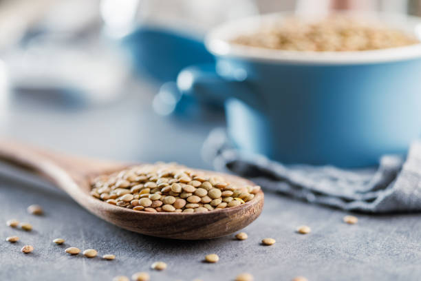 Uncooked lentil legumes in wooden spoon on kitchen table.