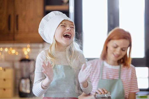 A cute girl with blond hair and chef's hat playing with flour in the kitchen