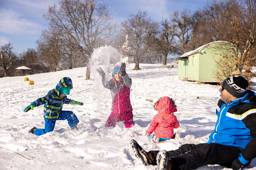 Caucasian family, parents with their children, playing in the snow, during an ski holiday on the mountain