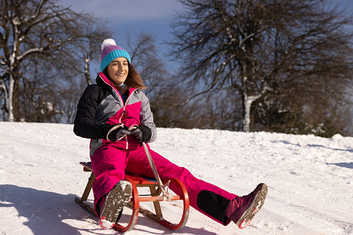 Excited young Caucasian woman sledding with sled on the small hill, during a winter day on the mountain