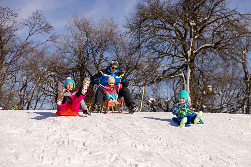 Caucasian family, parents with their children sledding on the hill with sled, during winter holiday