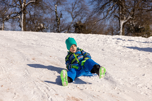Caucasian boy sledding with sled on the small hill, during a winter day on the mountain