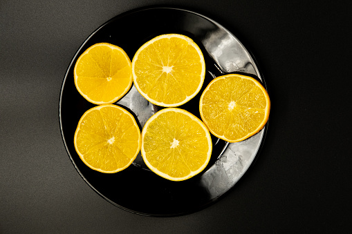 Photo of sliced ​​oranges in a black plate on a black background