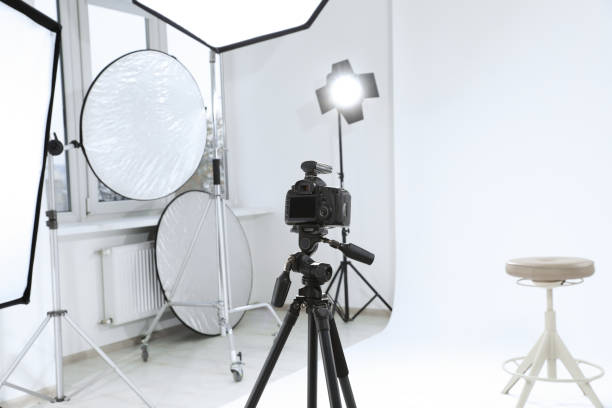 istock Tripod with camera, bar stool and professional lighting equipment in modern photo studio 1810147706