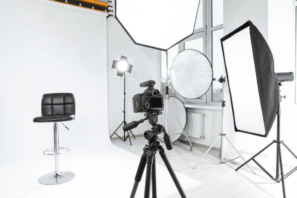 istock Tripod with camera, bar stool and professional lighting equipment in modern photo studio 1810148217